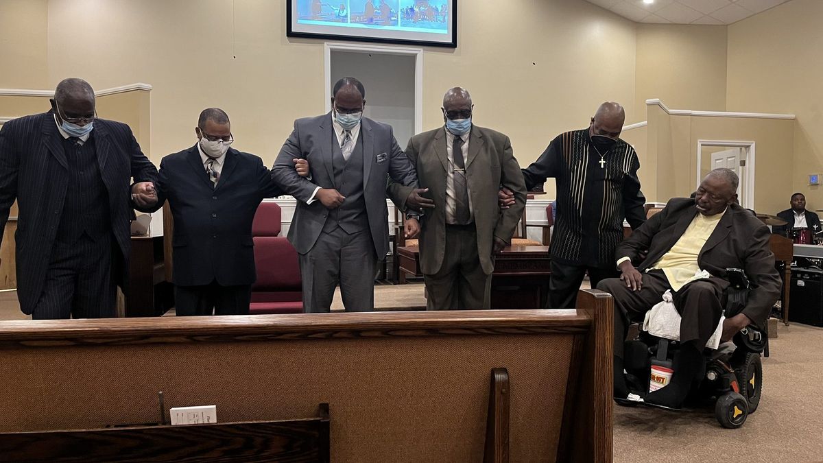 Men of Flint River Church linking arms in prayer at the front of the sanctuary